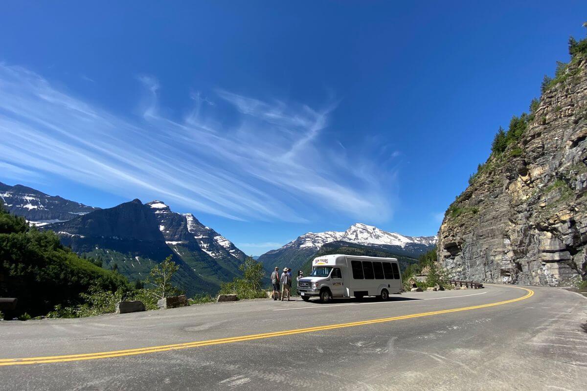 A white bus from Sun Tours parked by a mountain road with a scenic overlook during one of their Montana bus tours
