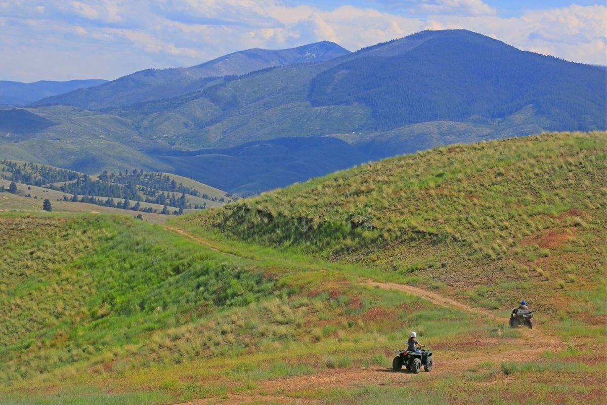 Two people on UTVs navigating a scenic off-road trail in a lush, rolling mountainscape 