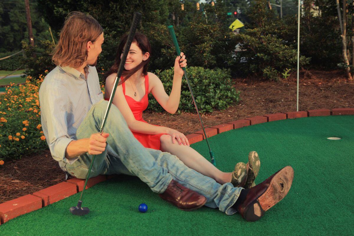 A man and a woman hold their putters as they sit down and take a break from their mini golf game at the Westside Lanes and Fun Center's mini golf course in Montana.