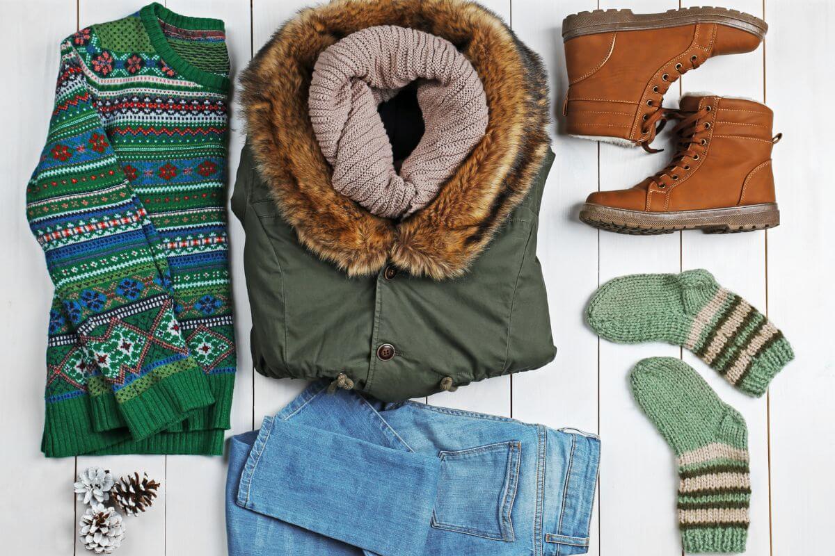 A cozy winter outfit featuring a sweater, jeans, and boots, laid out on a rustic wooden floor.