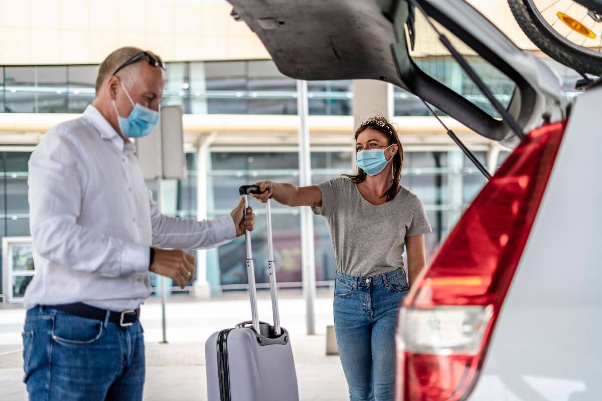 A man and woman wearing face masks are opening the trunk of a car in Montana.