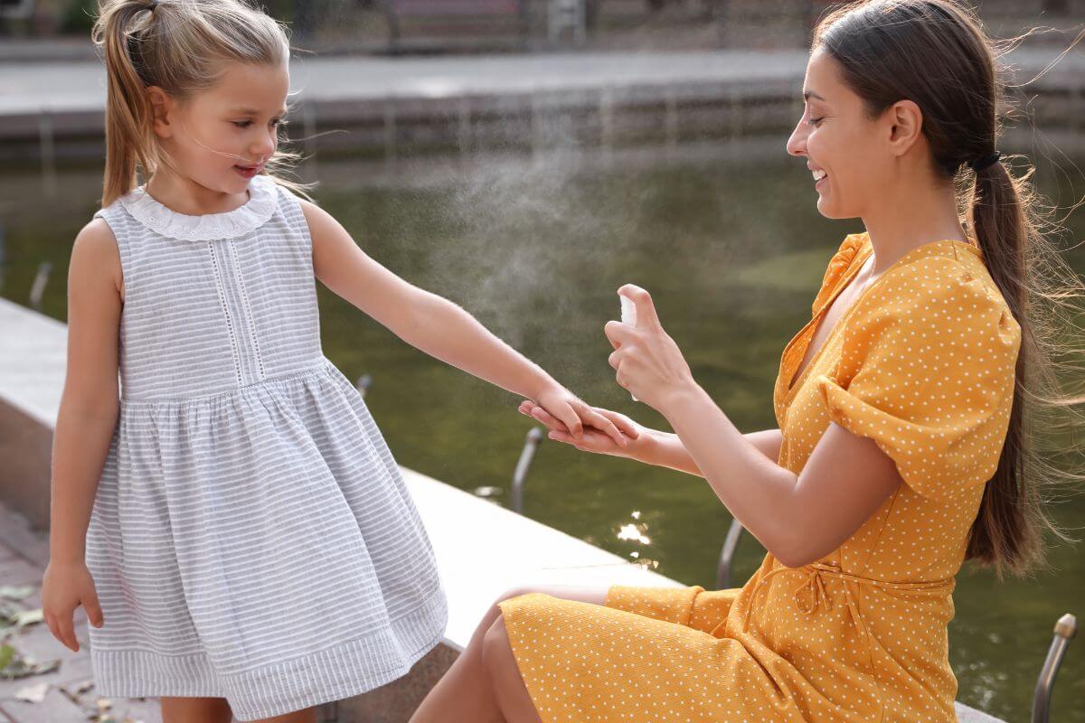 A woman spraying bug repellent on a little girl