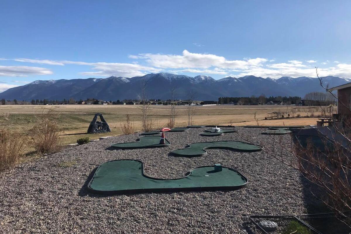 Holt State Hideaway's mini-golf course sits on a stony landscape beneath a clear, blue sky, with Montana mountains in the background.




