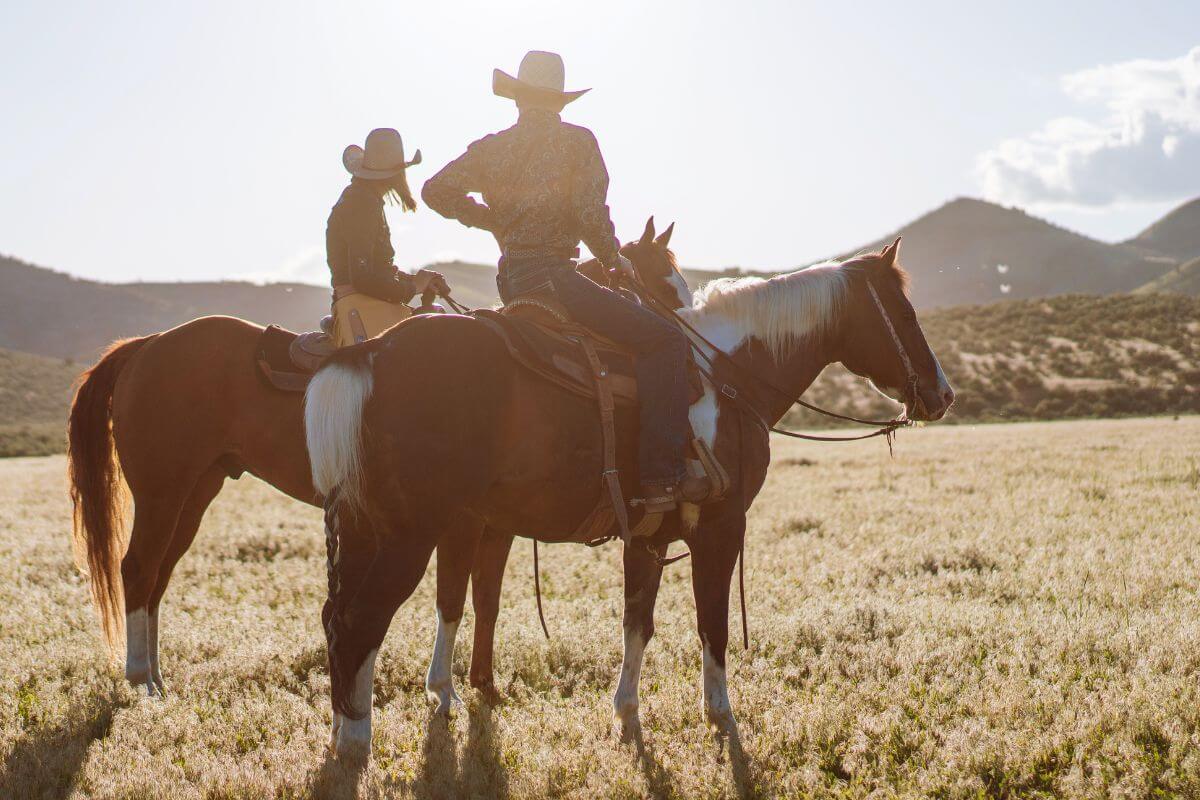A man and a woman dressed in cowboy outfits ride on horseback across the plains near Little North Fork Waterfall.