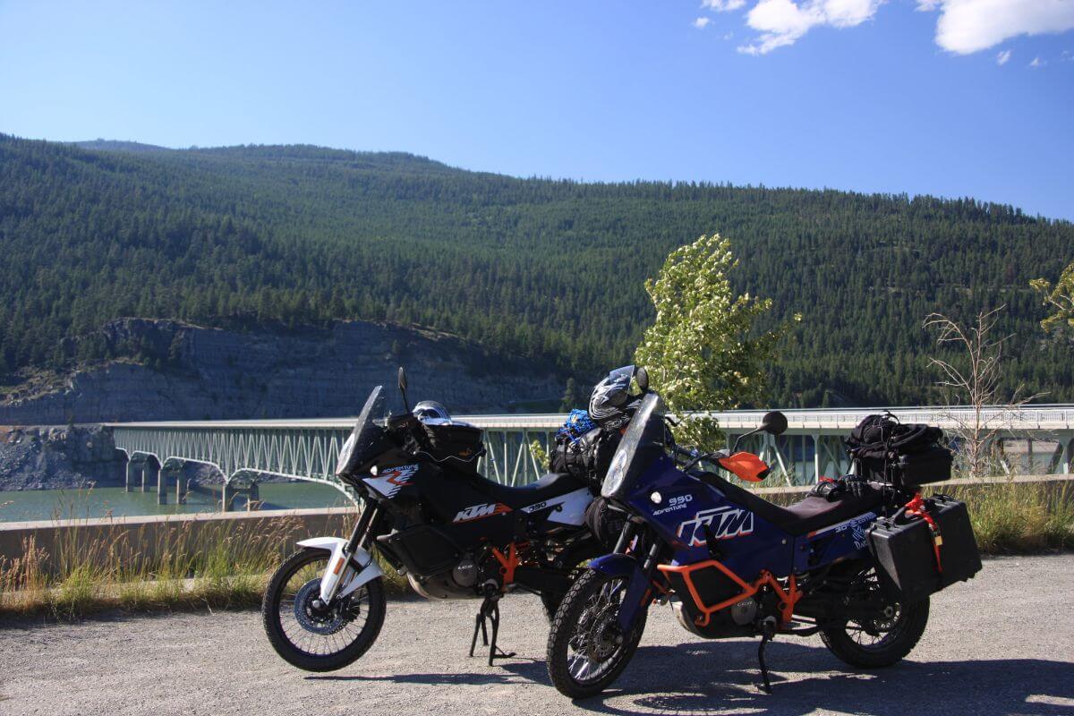 Two motorcycles parked on a scenic overlook with a view of forested mountains and Lake Koocanusa, during Montana motorcycle tours.