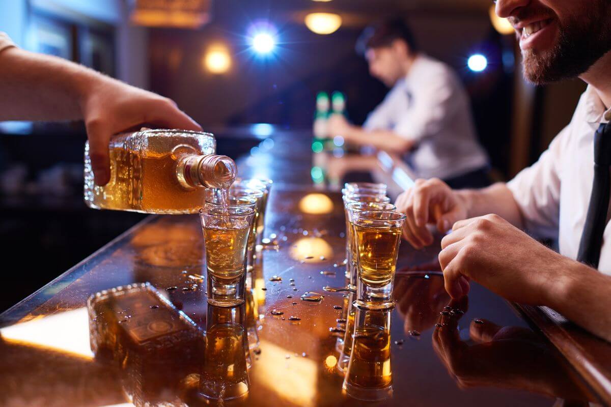 Man Pouring Alcohol in Ten Shot Glasses