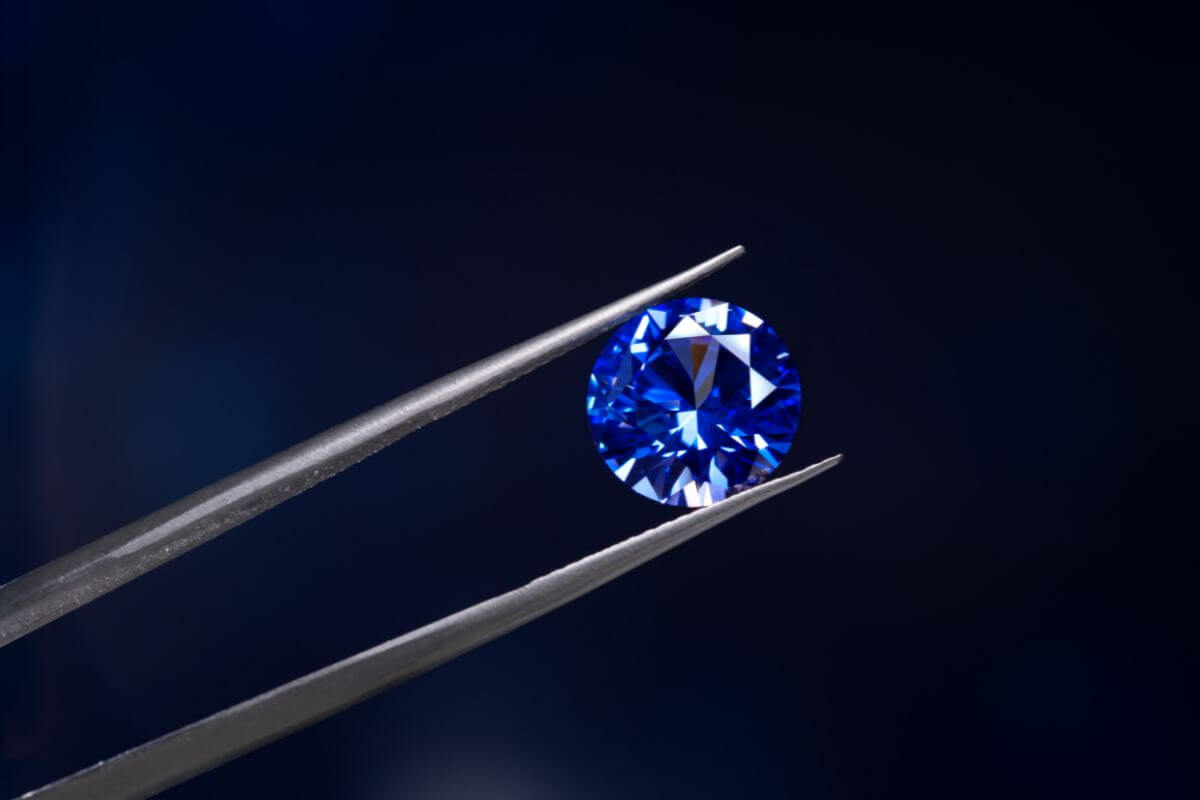 A sparkling blue Montana Yogo Sapphire delicately held by a pair of tweezers.
