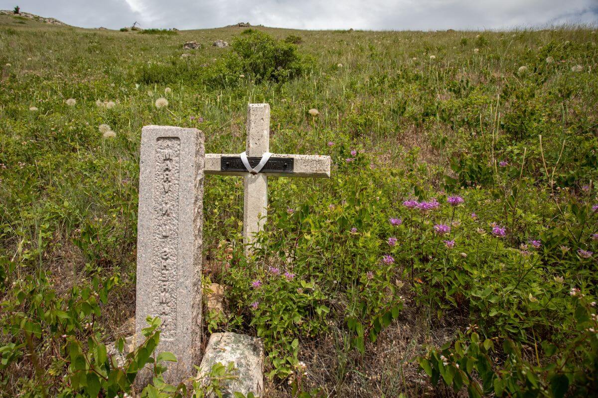 A cross and a tomb stone in the middle of a grassy hill in Montana.