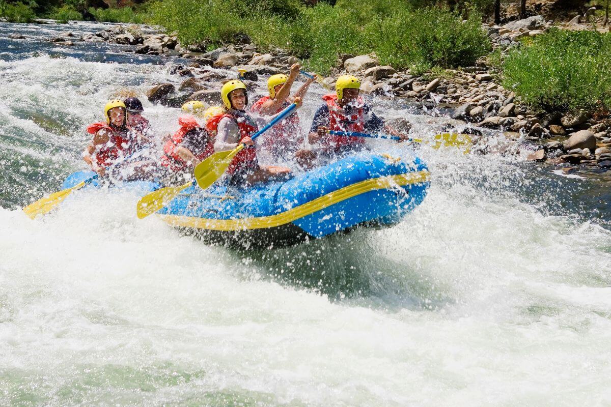 A group enjoys whitewater rafting through rough river rapids near Ipasha Falls on a bright yellow and blue raft.