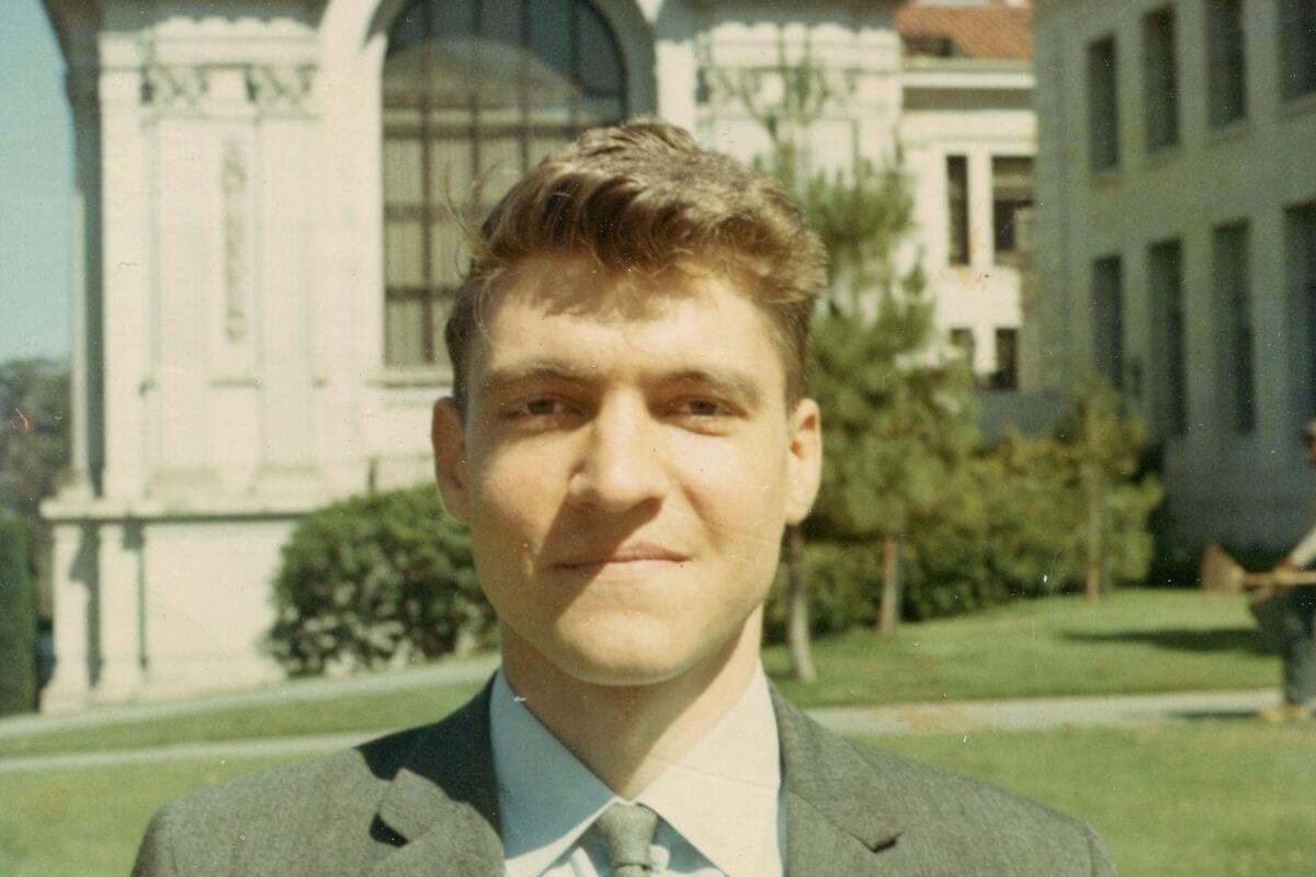 Young Theodore Kaczynski in a suit standing in front of a building in Montana.