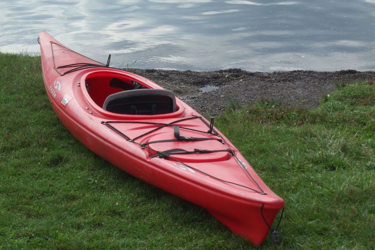 A red rental kayak rests on a grassy bank beside a lake in Glacier National Park.