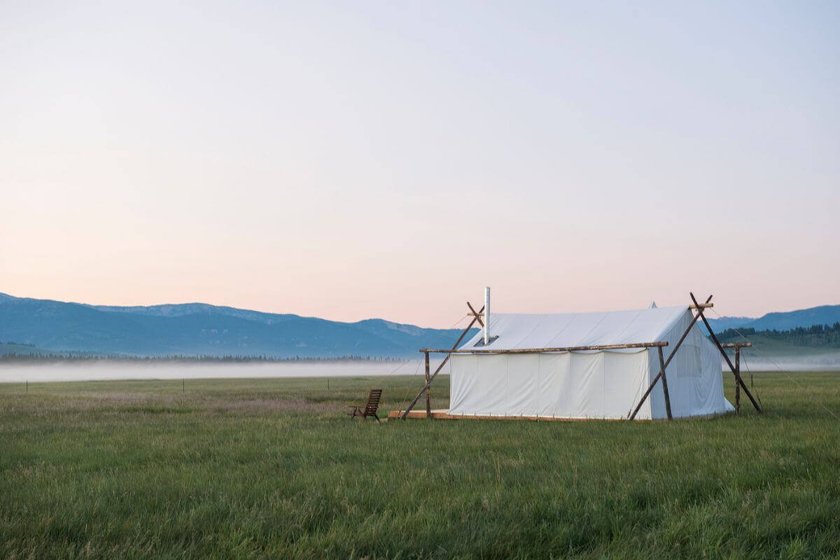 A tranquil tent nestled in the heart of Montana, surrounded by a vast field and majestic mountains in the distance.