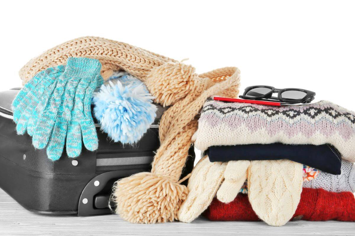 Winter clothing essentials, including mittens, gloves, hats, and scarves, are getting ready to be packed into a suitcase.