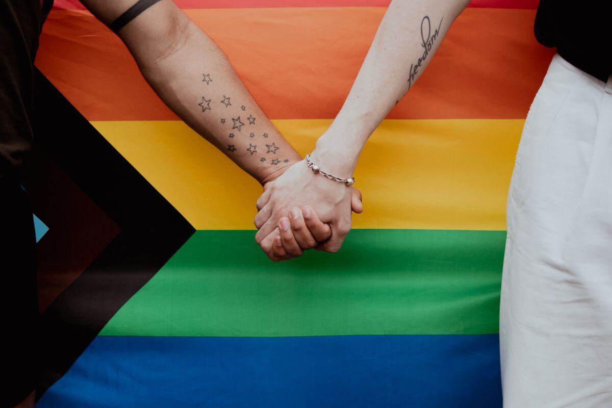 Two people holding hands in front of a rainbow flag