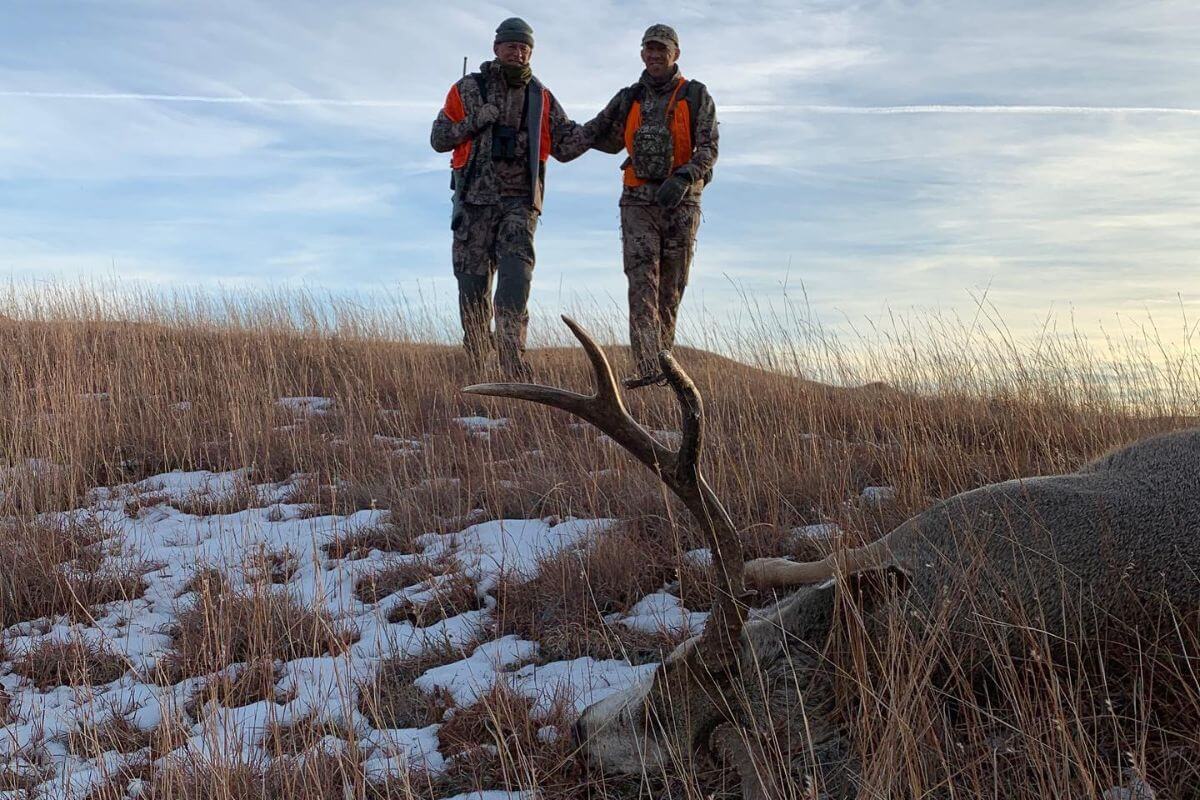Two hunters walk towards a deer they took down in the snowy wilderness of Montana.