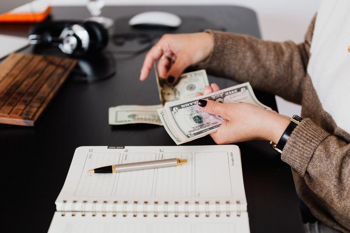 Woman Counting Money with Notebook and Pen