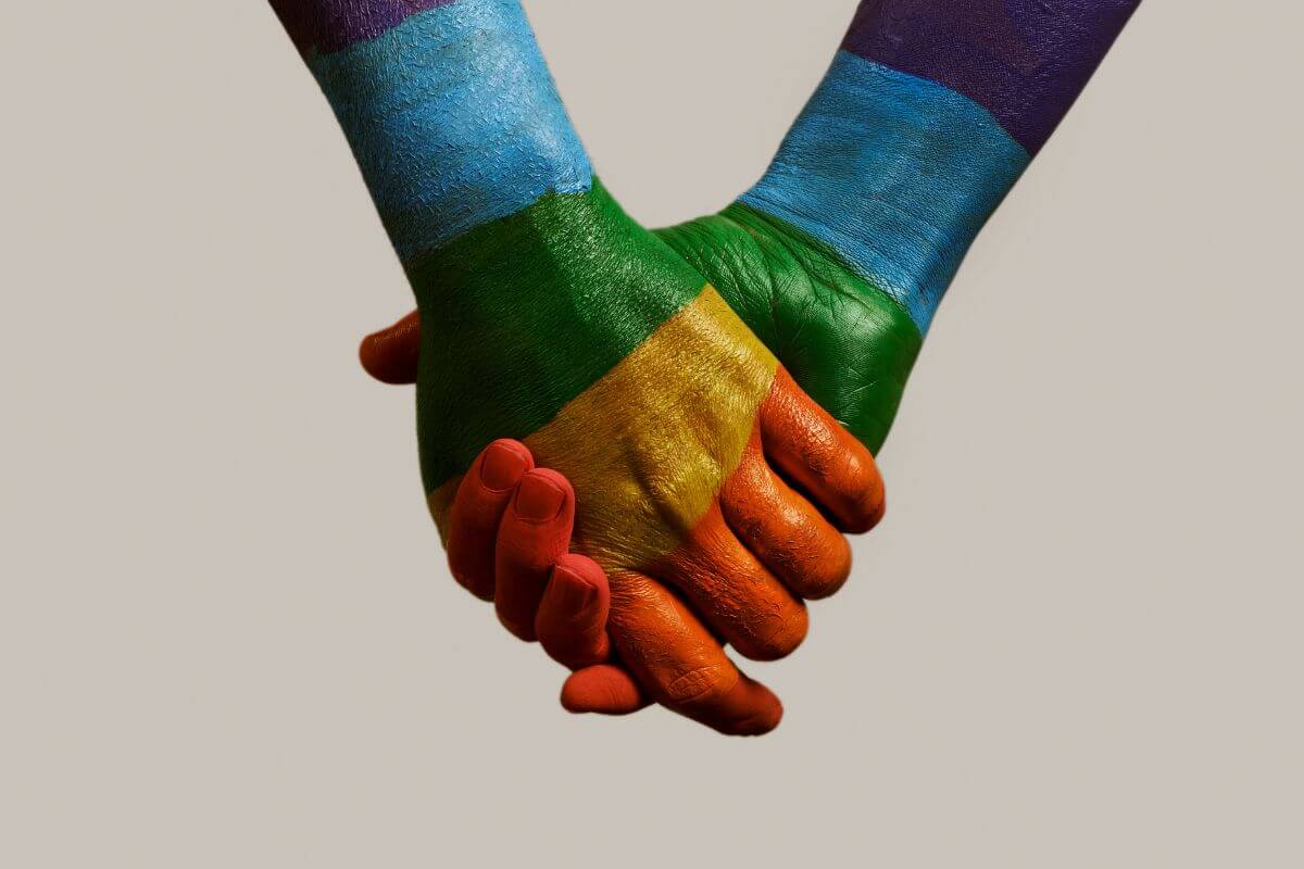 Two people holding hands painted in rainbow color representing LGBTQ pride