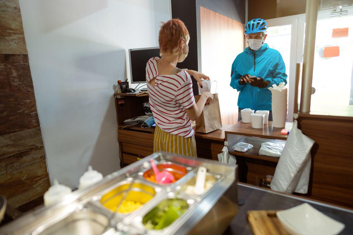 A woman in a mask prepares the food order of a customer, who is also in a mask, during the COVID-19 pandemic.