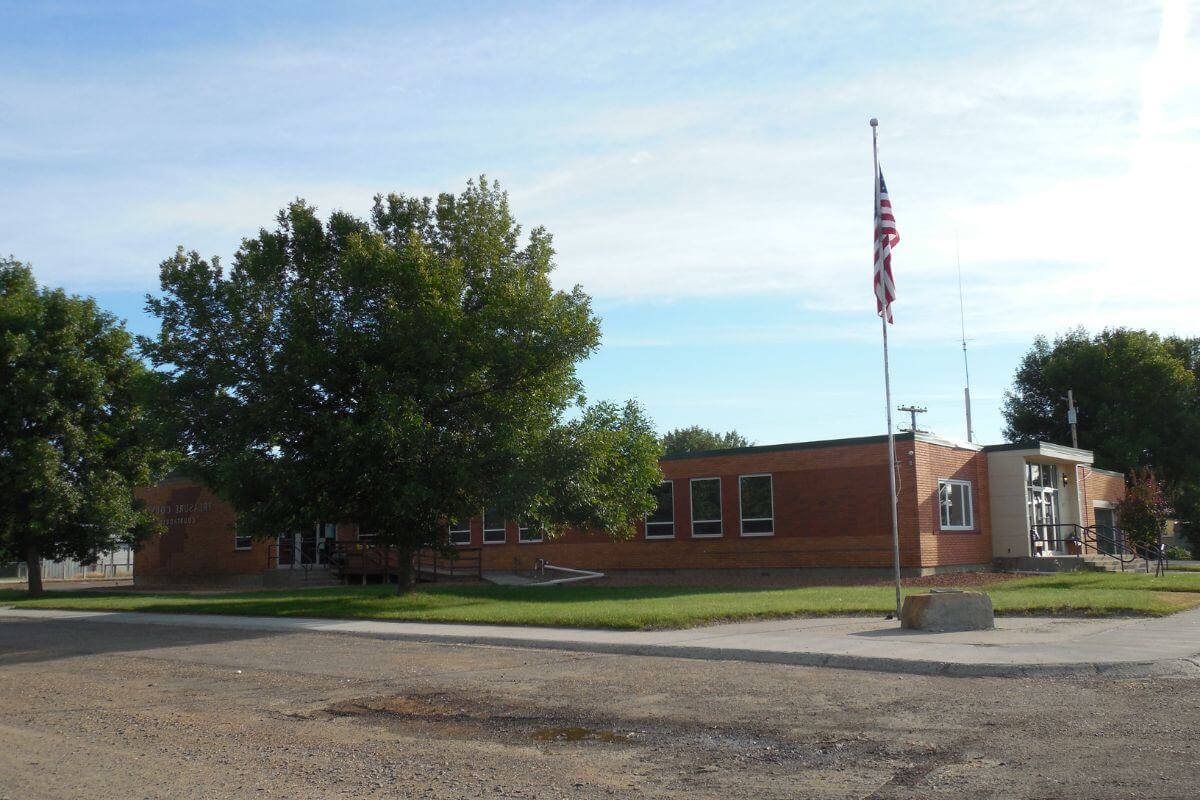 A brick building with an American flag in front of it in a rural location in Montana.