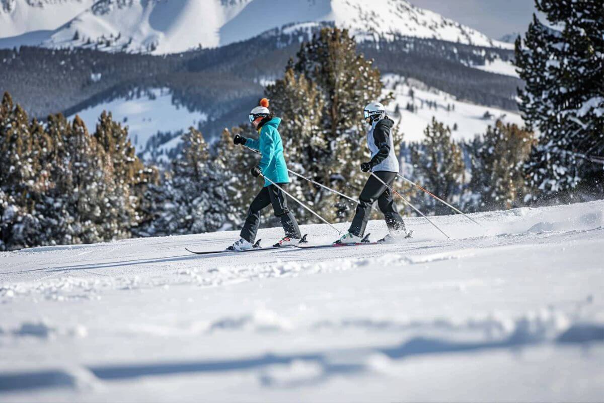 Two people skiing down a snowy slope with trees in the background in Montana.