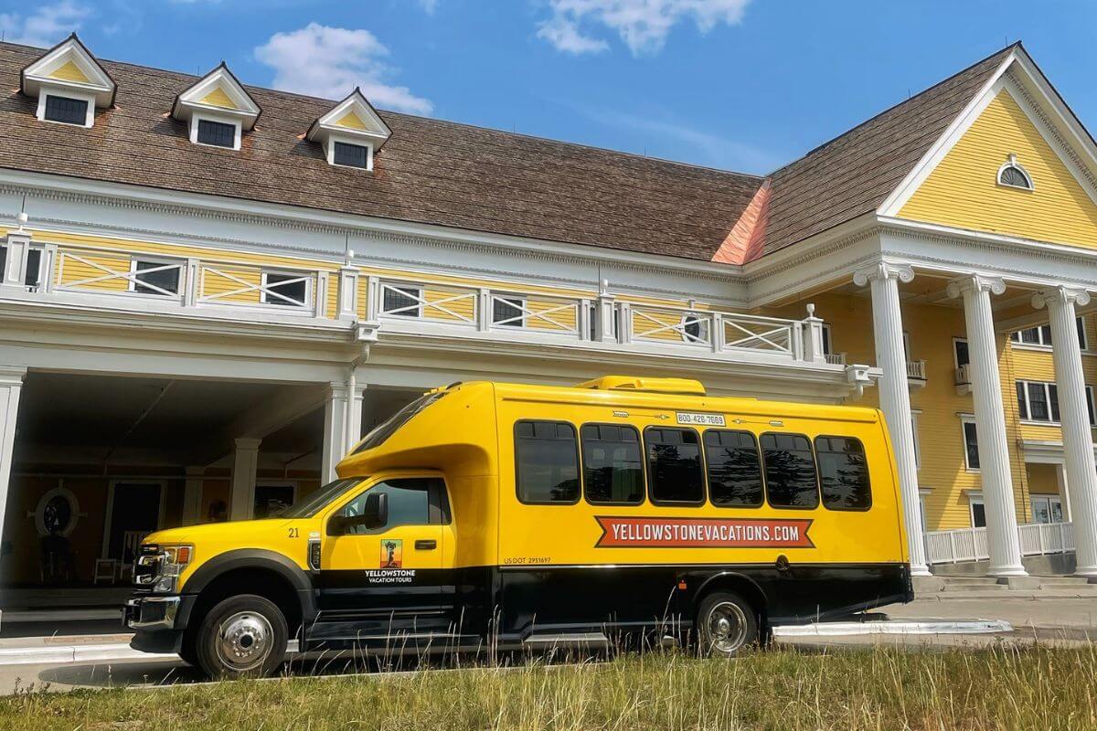 A yellow bus from Yellowstone Vacations parked in front of a white and yellow building in preparation for a bus tour.