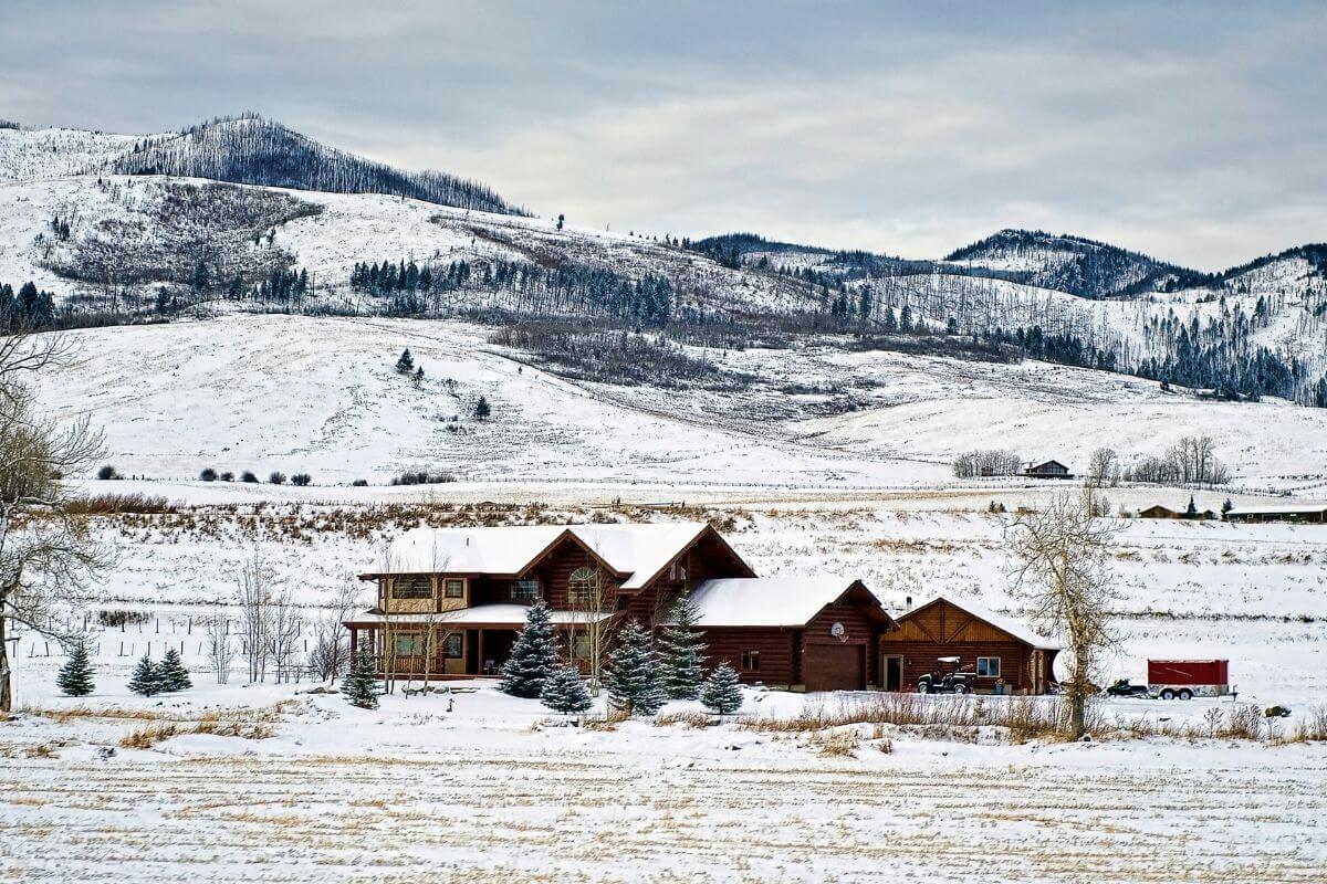 A house in the middle of a snowy field in Montana with mountains in the background