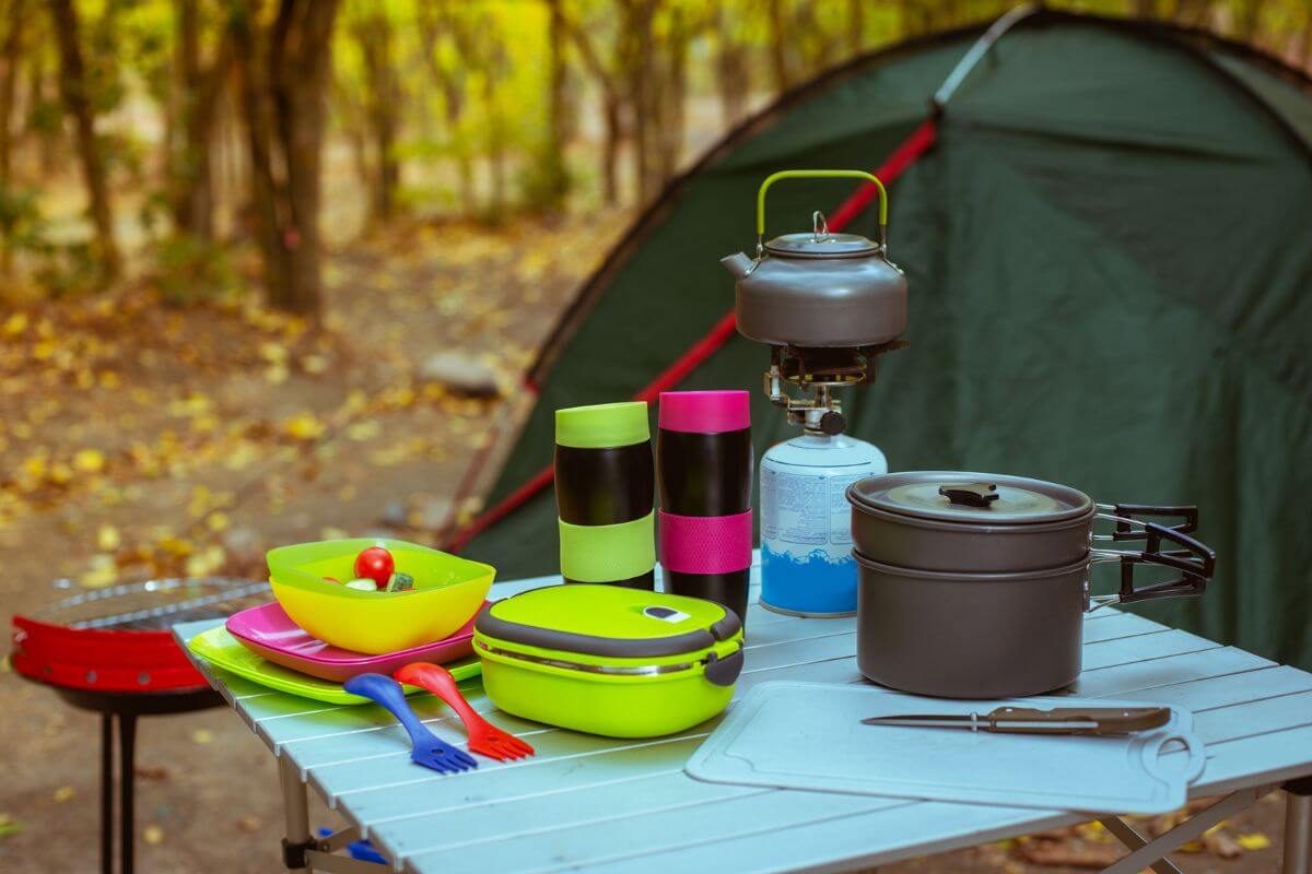 Camping cookware and colorful utensils set up on a table beside a tent in the woods near Impasse Falls.