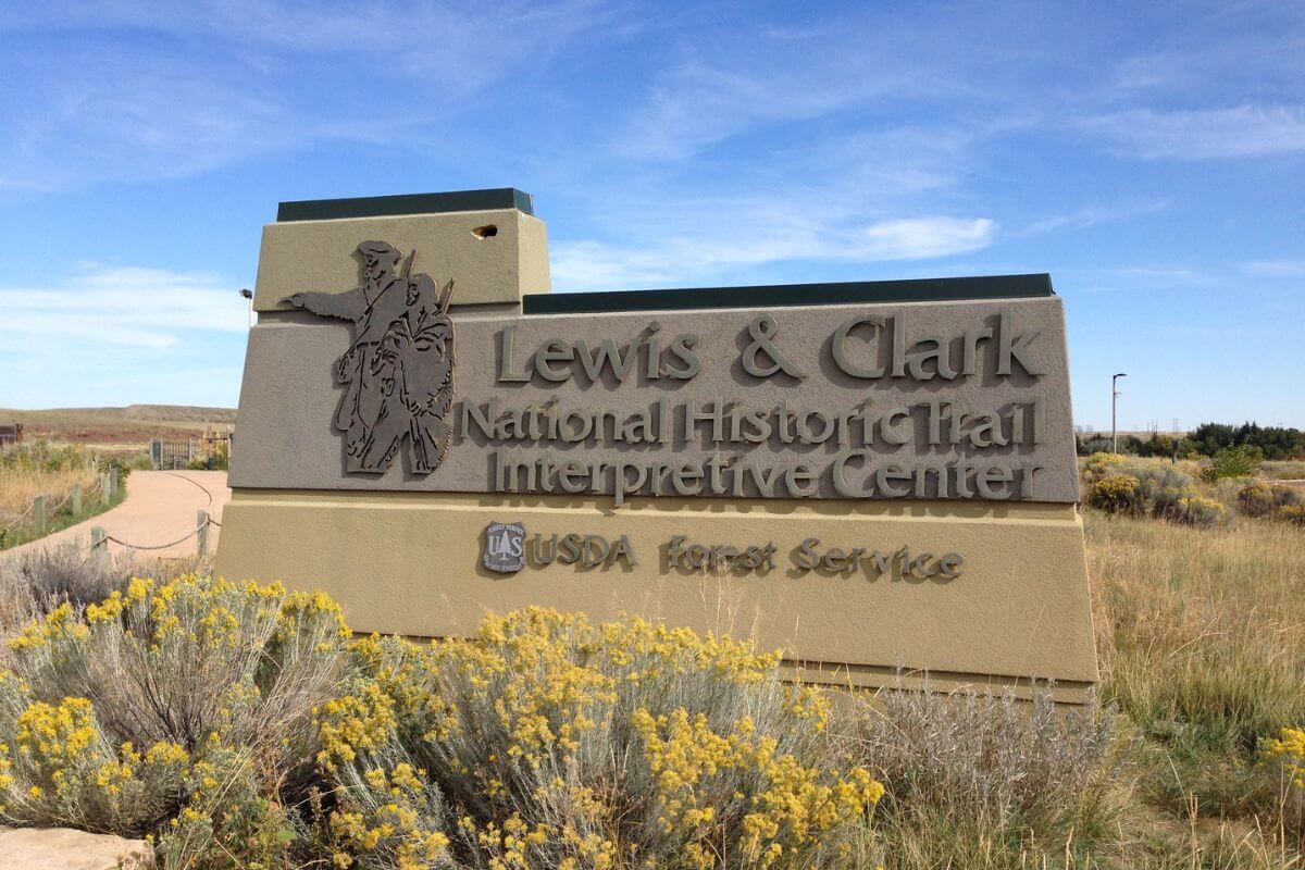 Lewis and Clark on the National Historic Trail sign surrounded with bushes under a clear sky.