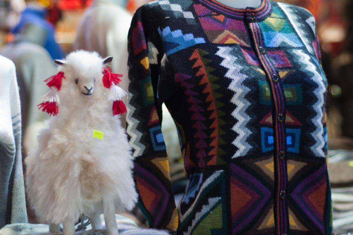 A colorful sweater made of Montana alpaca fleece is displayed beside a small alpaca toy statue.