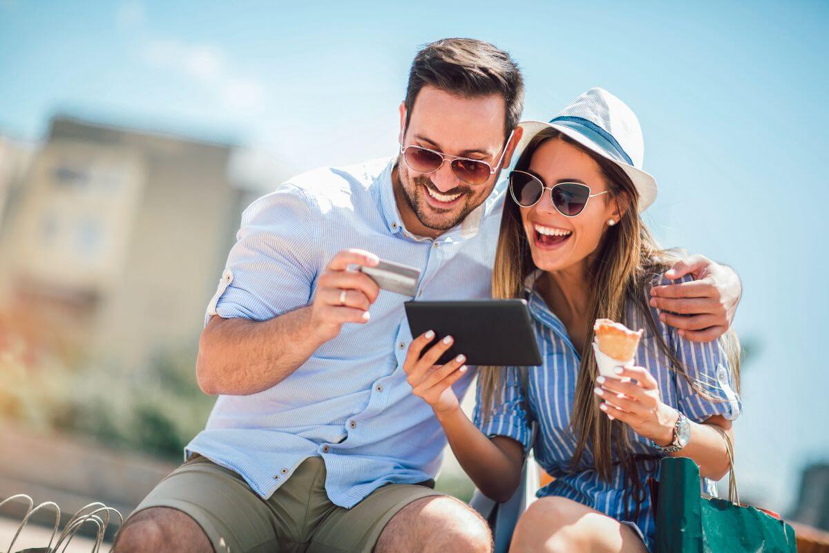 A man holds his credit card while a woman, enjoying ice cream, holds her phone as they enjoy their Montana trip.