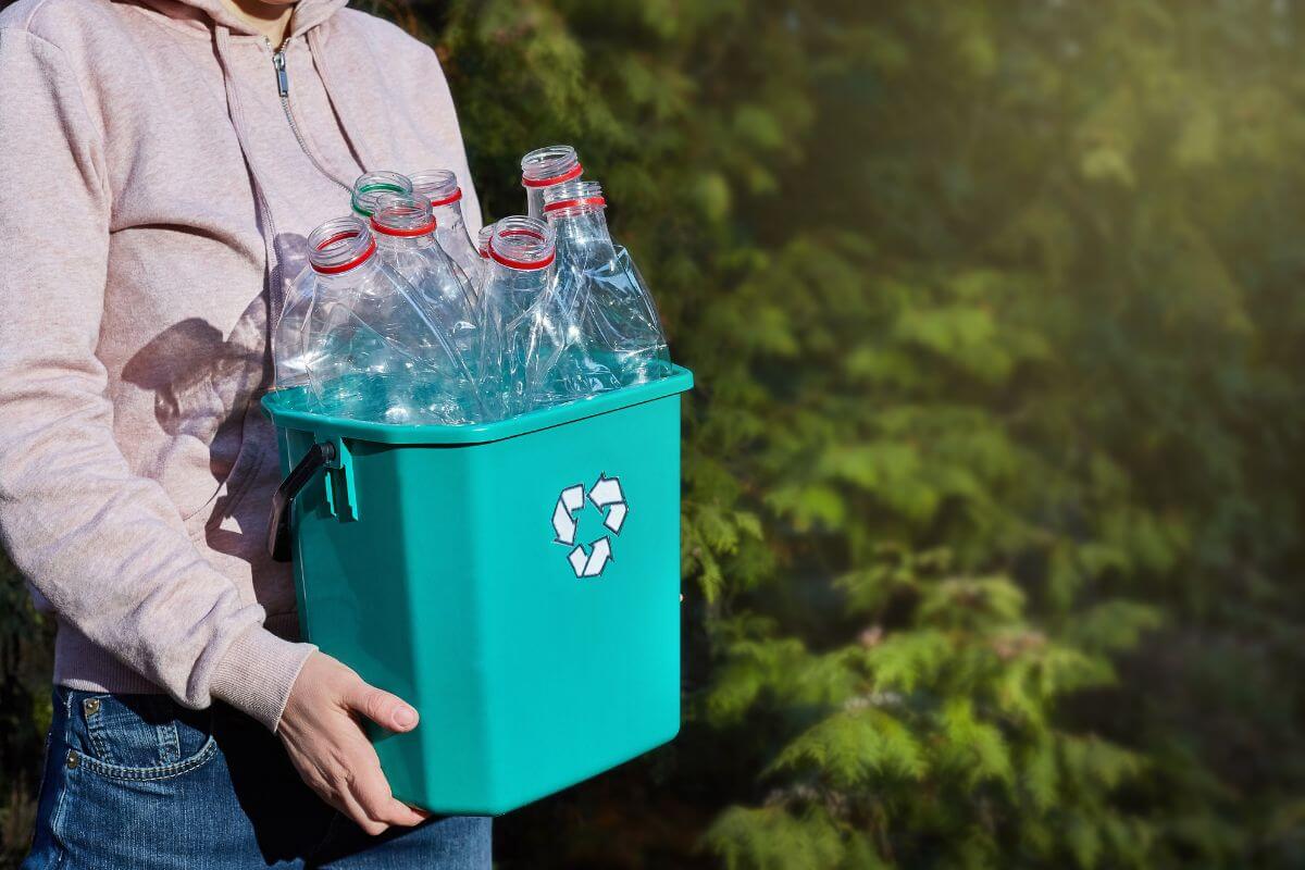 A woman holding a green recycling bin full of plastic bottles