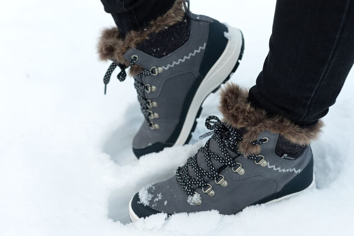 A woman wearing stylish winter boots stands with one foot on tiptoe in the snow in Montana
