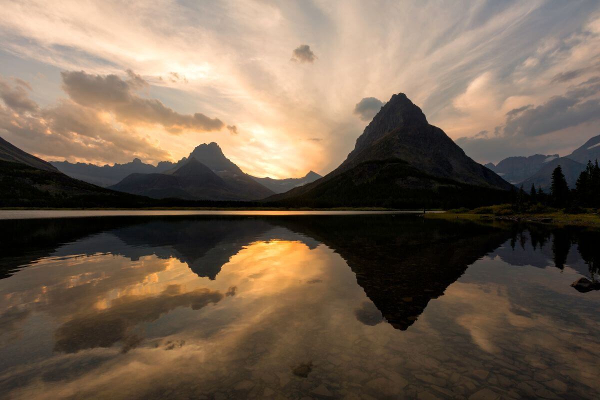 A sunset in Montana casts a reflection of a mountain range on a serene lake.