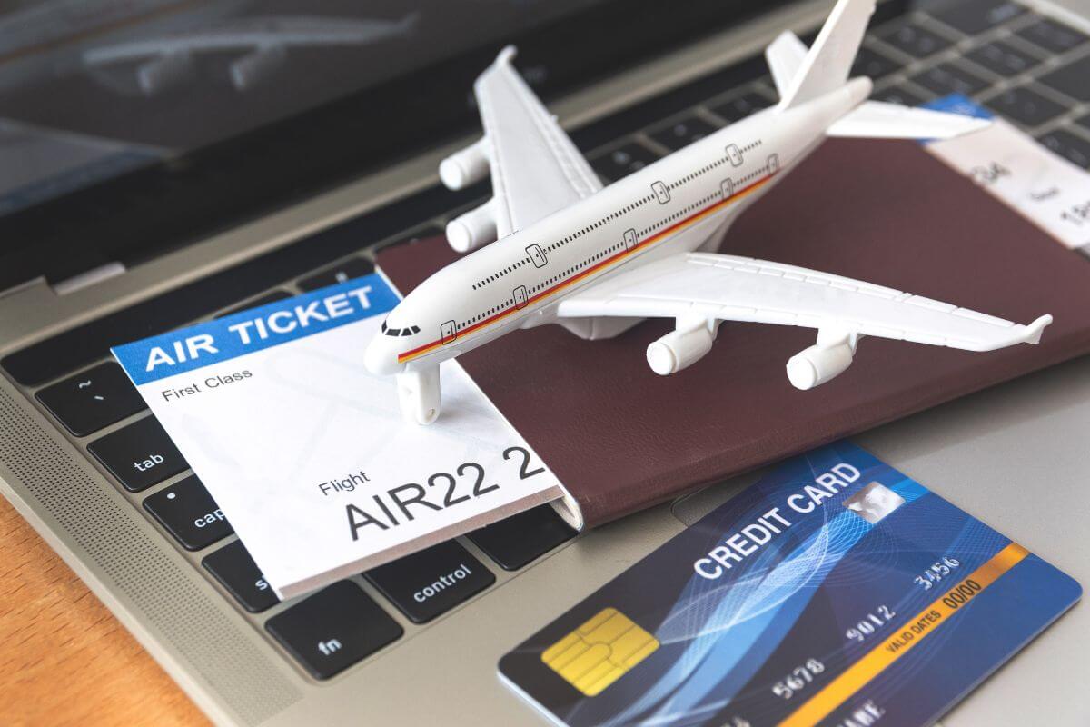 A model airplane, passport, plane ticket, and credit card sit casually on top of a laptop.
