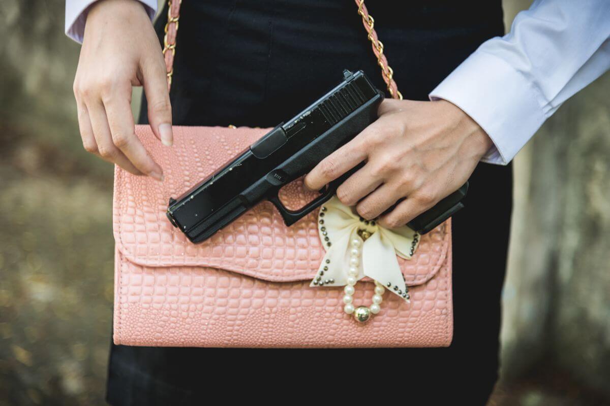 Woman Holding a Gun Near Pink Purse