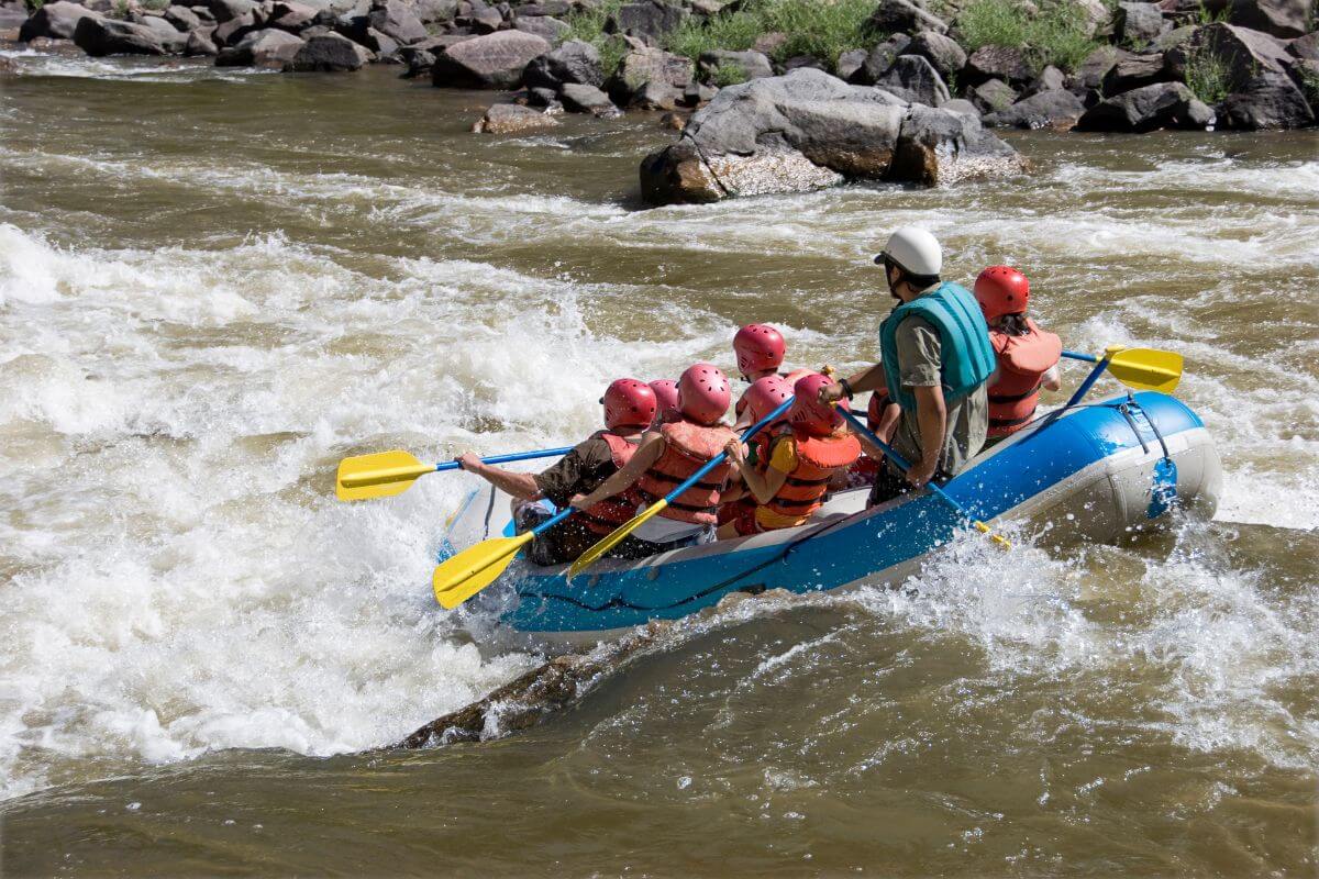 A group of adventurers brace themselves as their white water raft enters the rushing rapids of a river.