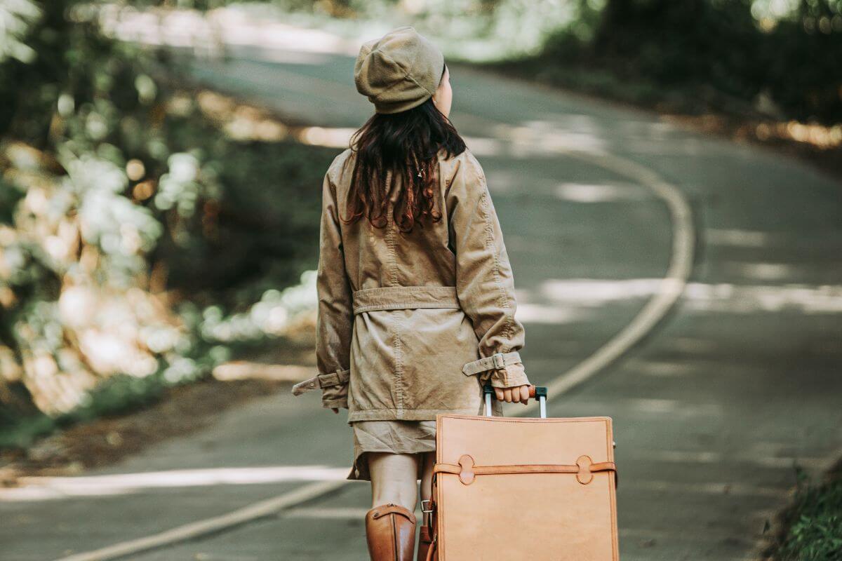 A woman is walking down a road in Montana with a suitcase.