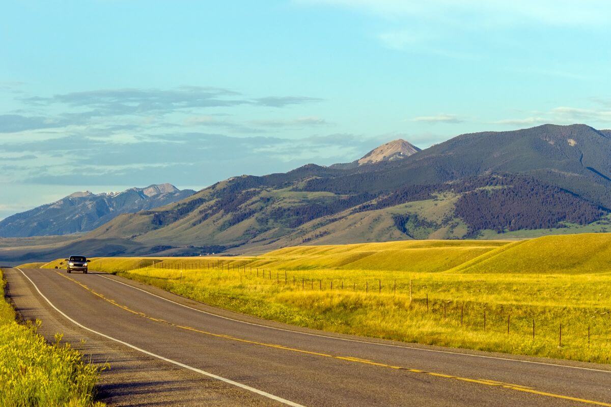 A truck driving down a road with Montana mountains in the background.