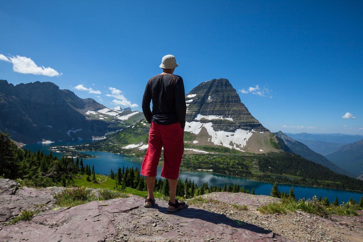 A person stands on a rocky ledge, admiring the unique, breathtaking view of a clear lake in Glacier National Park.