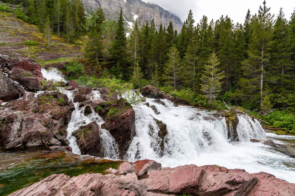 Greenery surrounds the rushing Redrock waterfall tumbling over rugged terrain in Montana's mountains.