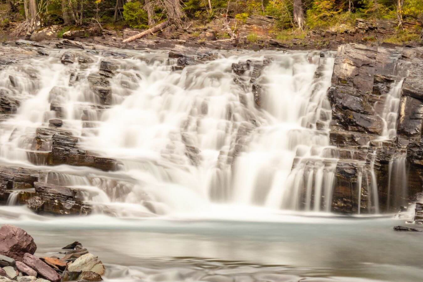 Sacred Dancing Cascade flows over tiered, rocky ledges surrounded by forested banks.